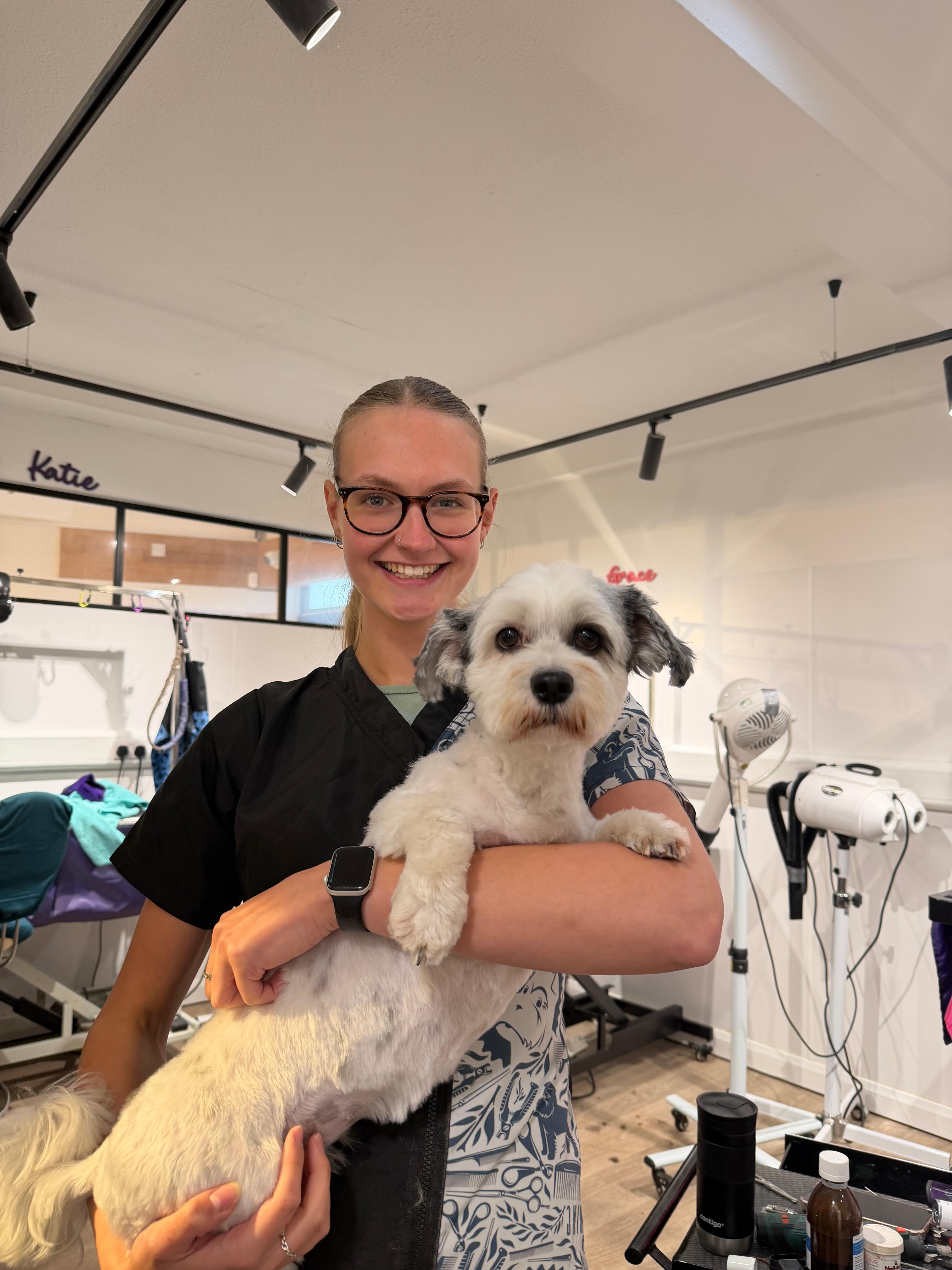 A groomer holding a small white dog after its groom